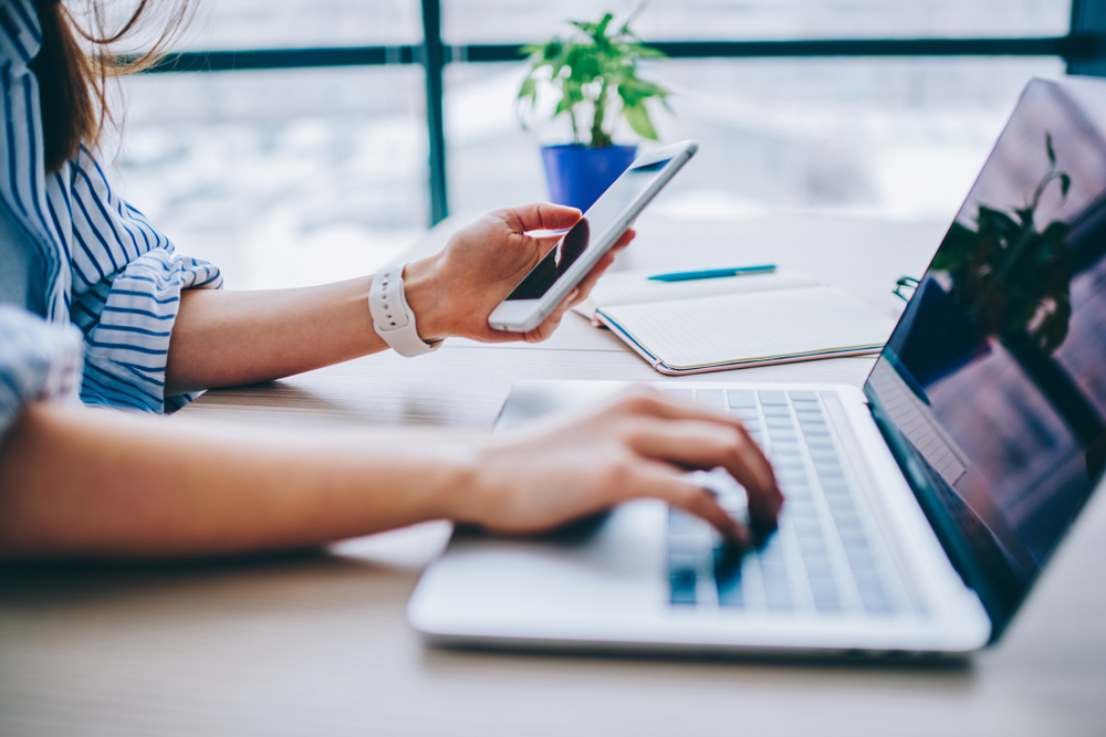 A Woman Is Typing On the Laptop and Holding a Mobile Phone